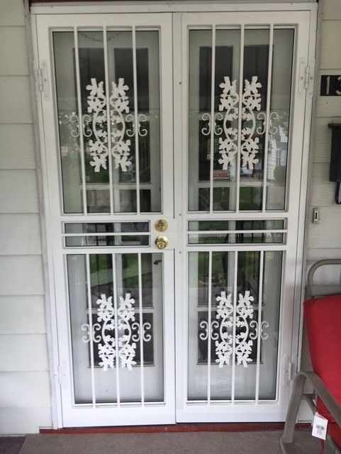 White double front doors with decorative snowflake decals and metal security bars on a porch.
