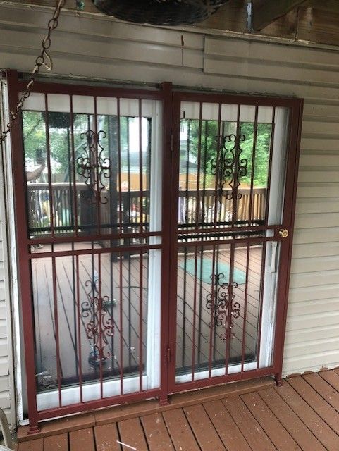 White metal security doors with decorative bars on a porch, opening to a green outdoor view.