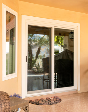 Sliding glass doors opening to a patio with potted plants and a covered grill Sliding glass doors opening to a patio with potted plants and a covered grill