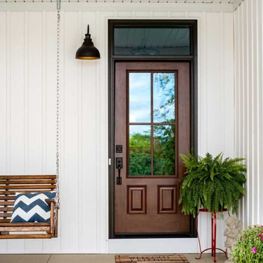 Front porch with brown door, black lantern, wicker swing, and potted fern against white siding Front porch with brown door, black lantern, wicker swing, and potted fern against white siding