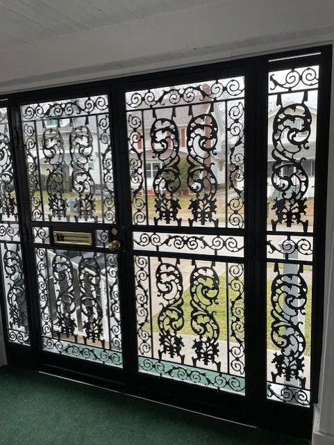 Ornate black wrought-iron gate with frosted glass panels and scrolling floral designs at an entrance