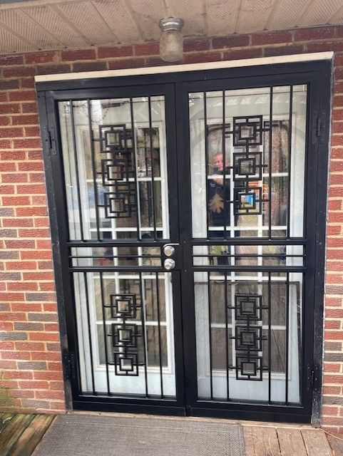 Black metal security double doors on a brick house porch with glass and decorative grille panels