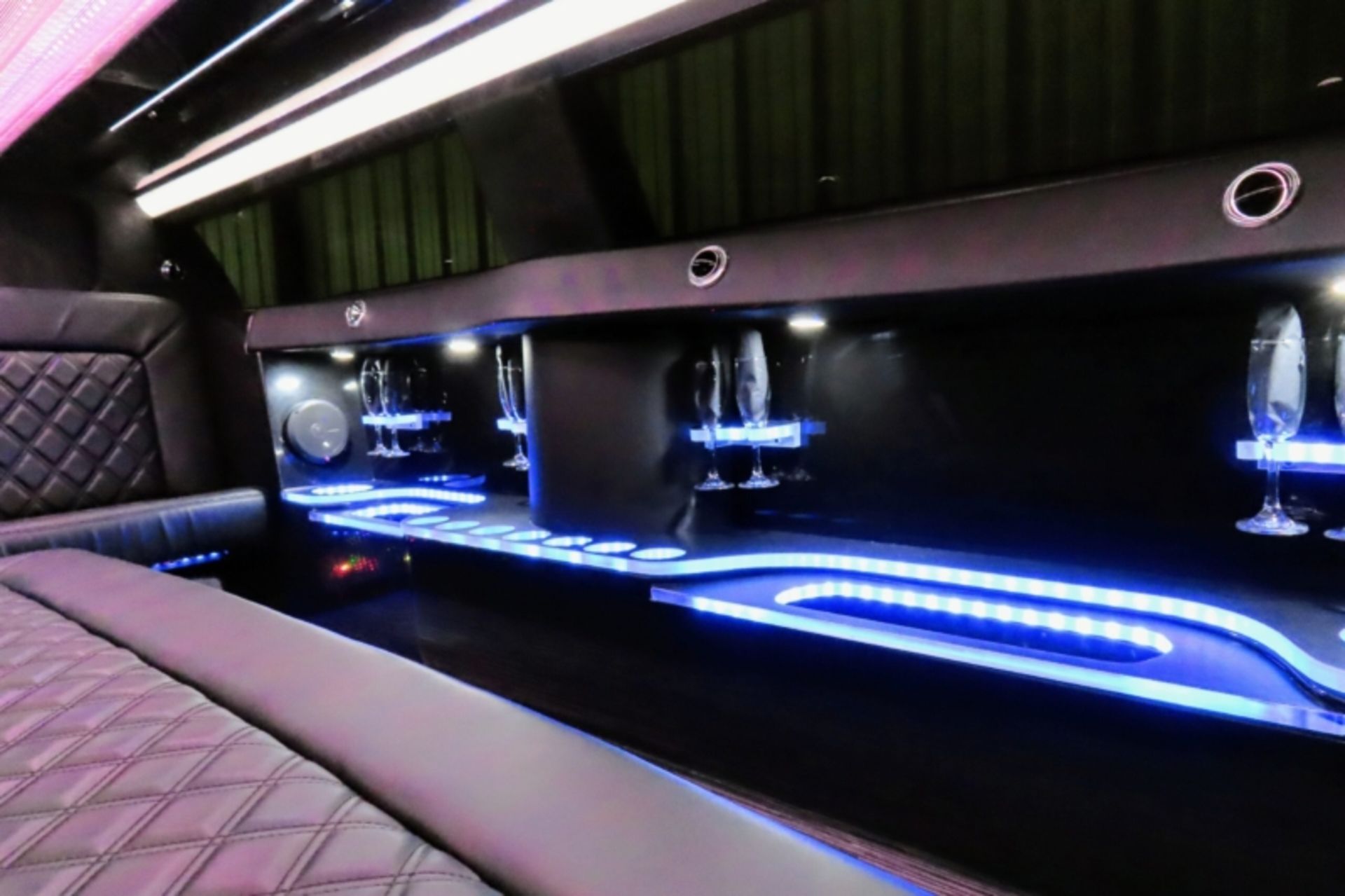 Inside a limousine, a bar area is illuminated with blue lights. 