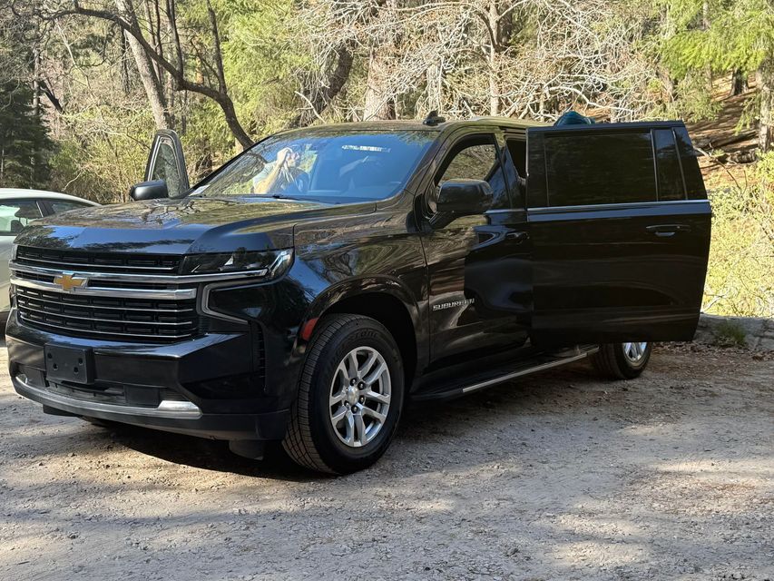 Black Chevrolet SUV parked on gravel with driver's side door open.  The setting is outdoors, trees visible in the background.