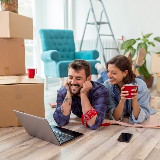 A man and a woman are laying on the floor using a laptop.