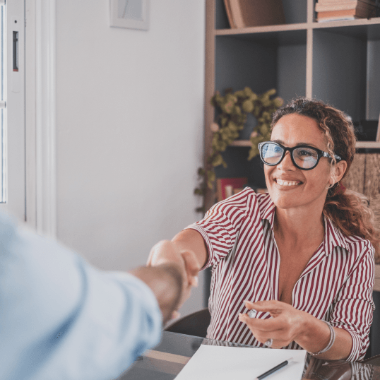 A woman is shaking hands with a man while sitting at a table.