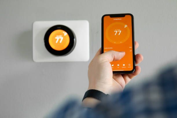 a person is holding a cell phone in front of a thermostat .