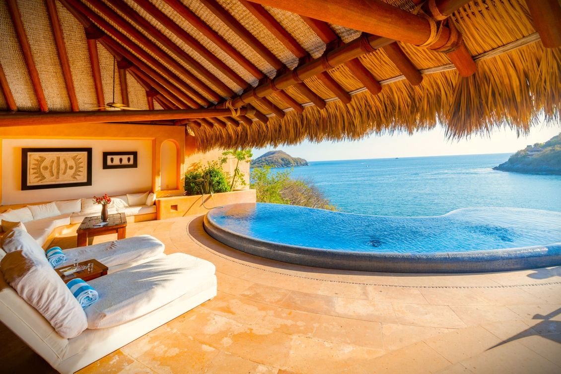 Villa frente al mar con piscina, sofás blancos, techo de paja, vista al mar.