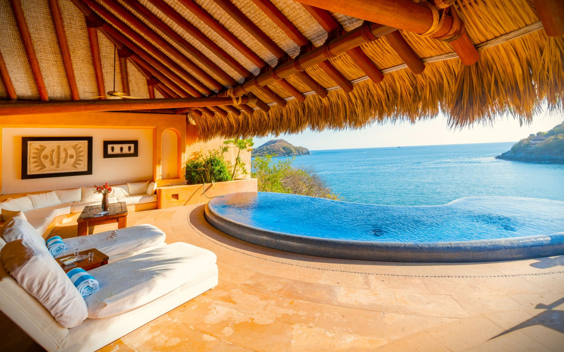 Villa frente al mar con piscina, sofás blancos, techo de paja, vista al mar.
