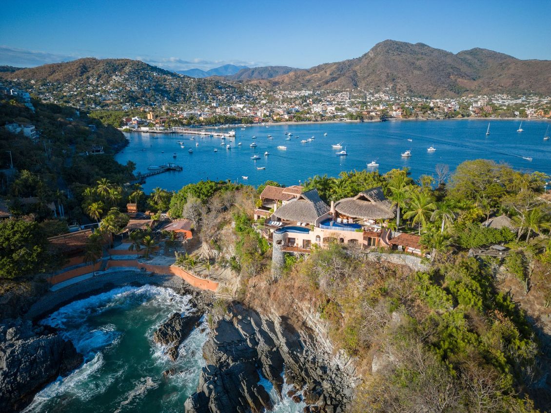 Villa costera con vistas a una bahía con barcos y montañas al fondo.