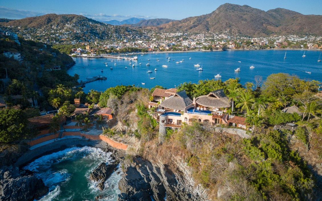 Villa costera con vistas a una bahía con barcos y montañas al fondo.