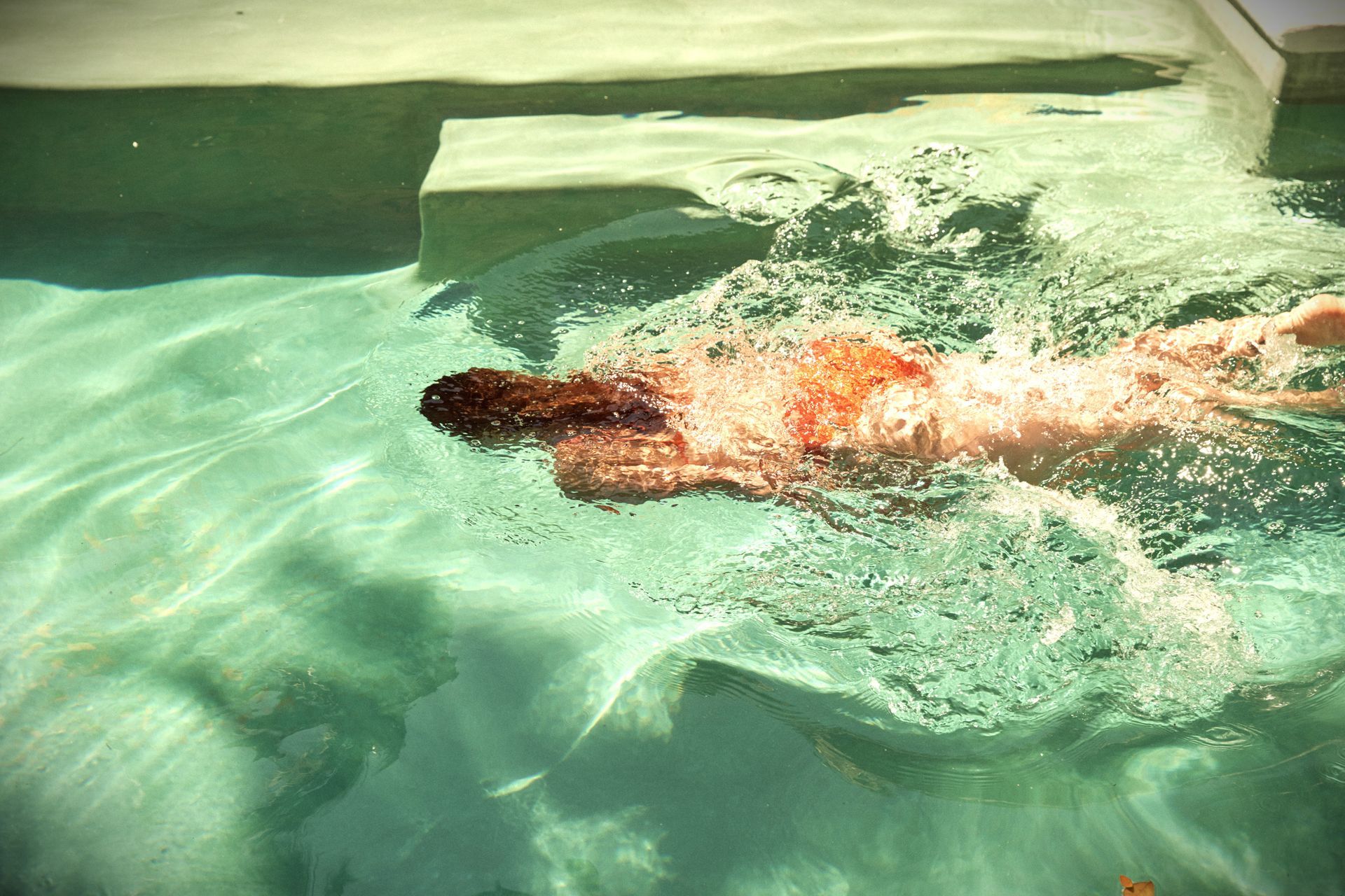 Mujer nadando en una piscina de color turquesa claro, con el cabello colgando detrás.