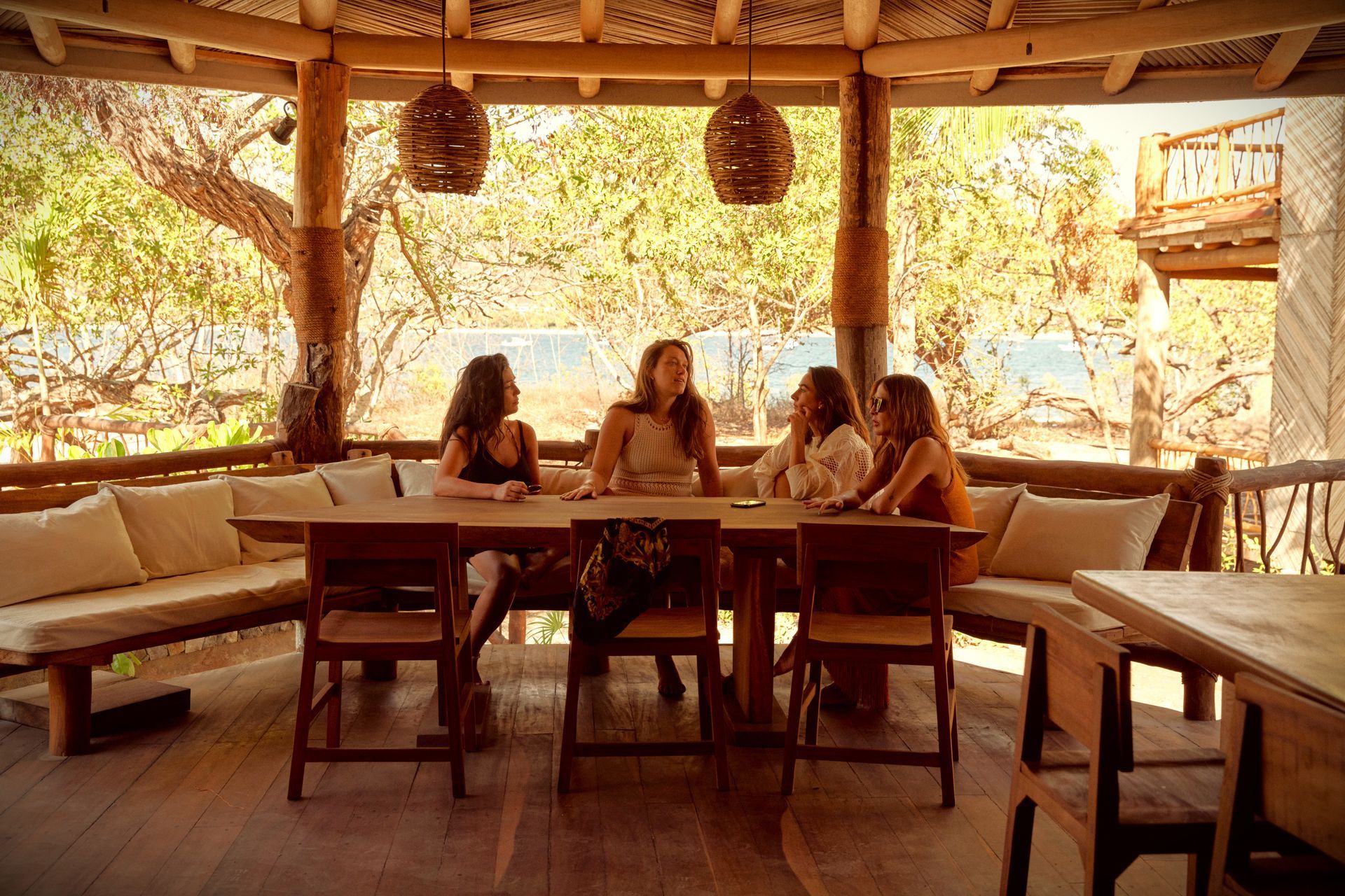 Cuatro mujeres conversan sentadas en una mesa de madera en un patio. Día nublado.