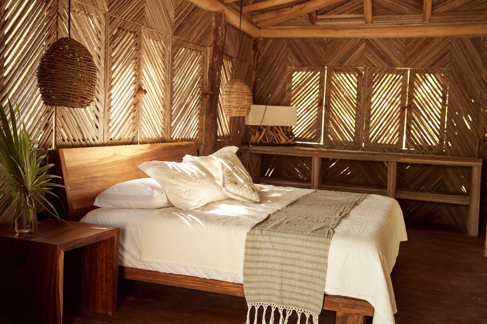 Bedroom with wooden bed, woven walls, and natural light.