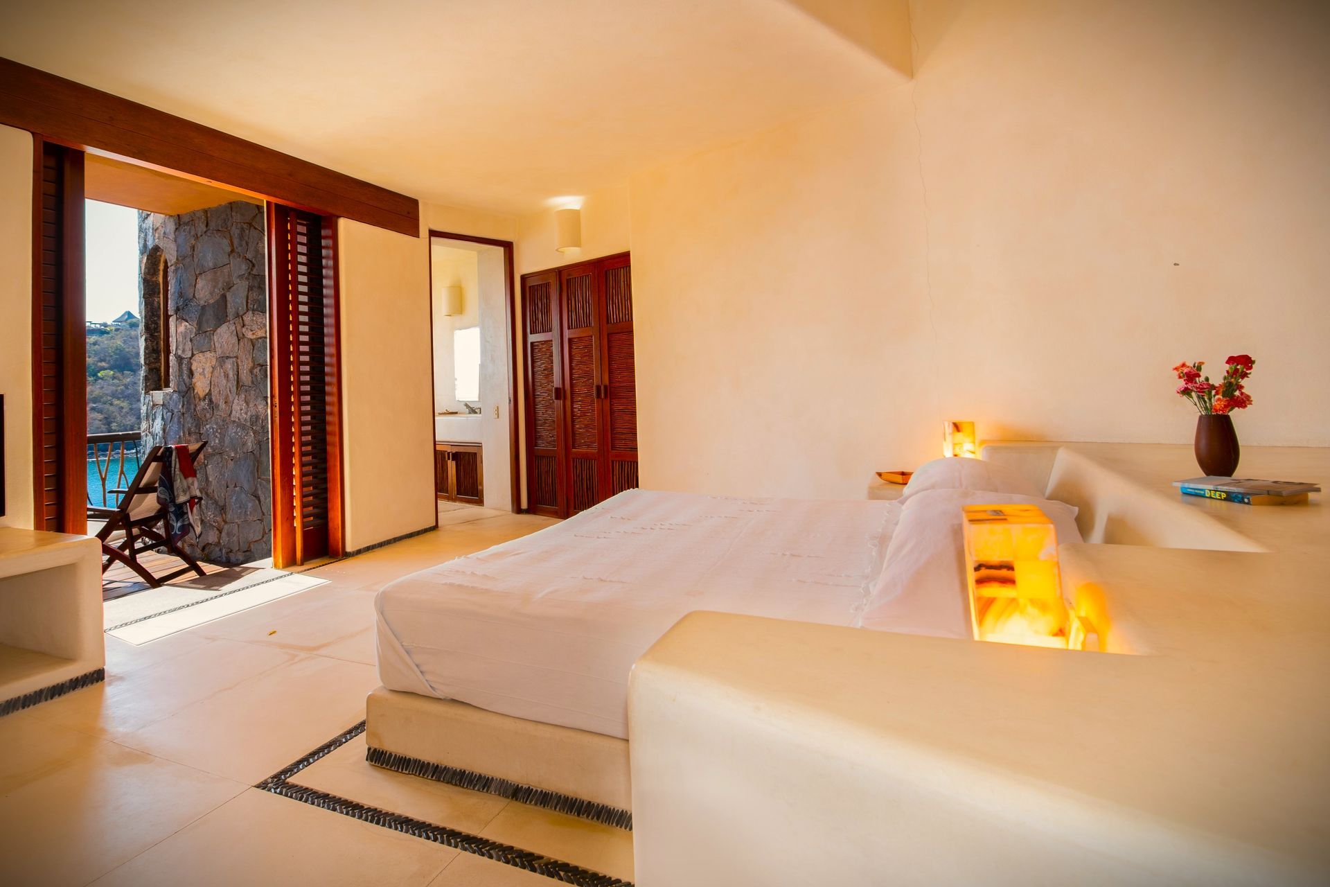 Bright hotel room with a bed, balcony, and view of the ocean.
