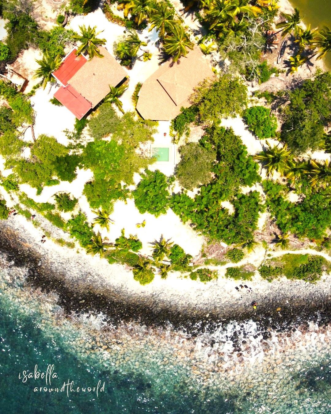 Vista aérea de isla tropical con dos edificios y exuberante follaje verde; océano en el fondo.