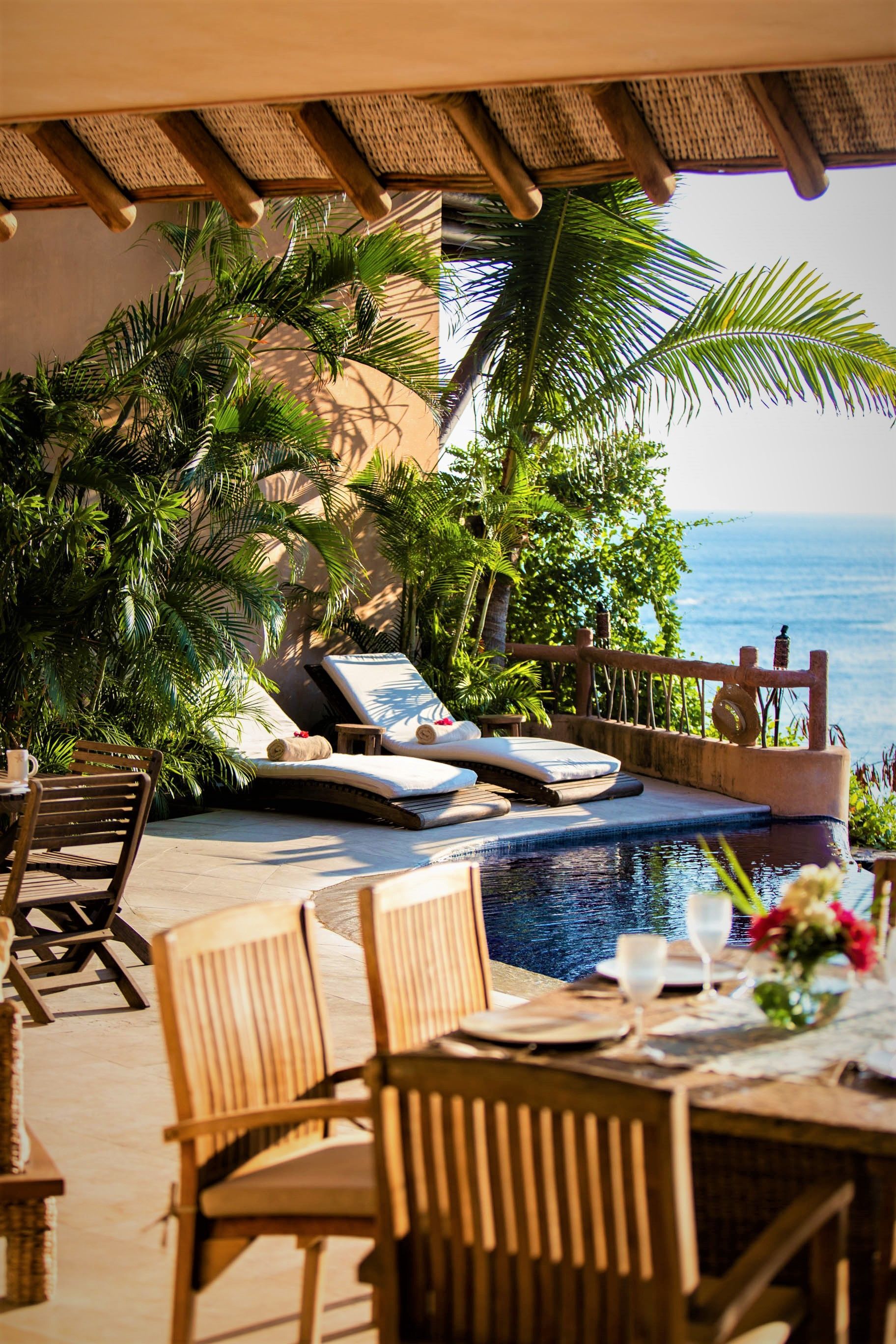 Patio con mesa y sillas, piscina y camastros con vista al mar.