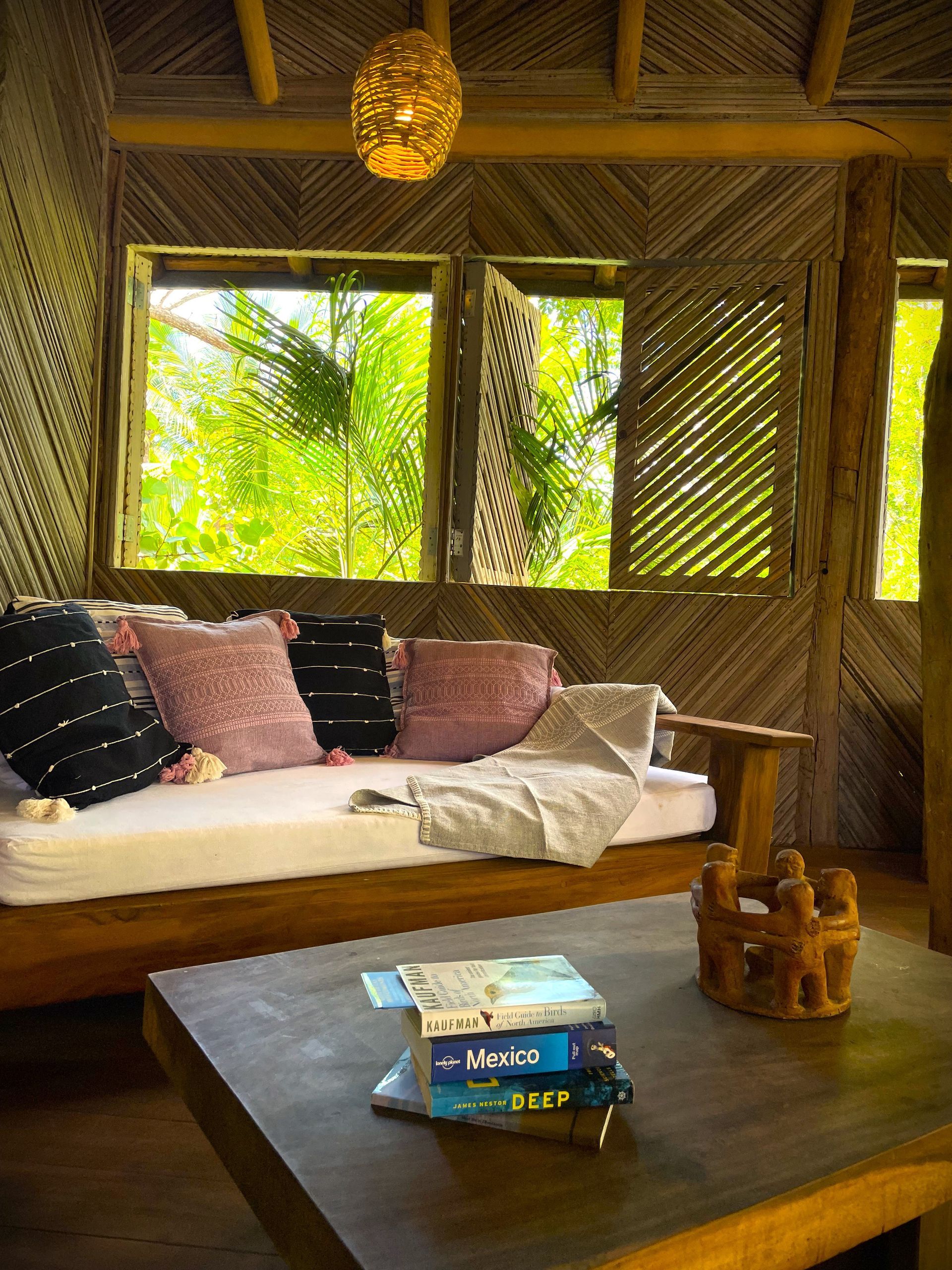 Habitación con estructura de madera, ventanas con vistas a la vegetación, un sofá y una mesa de café con libros.