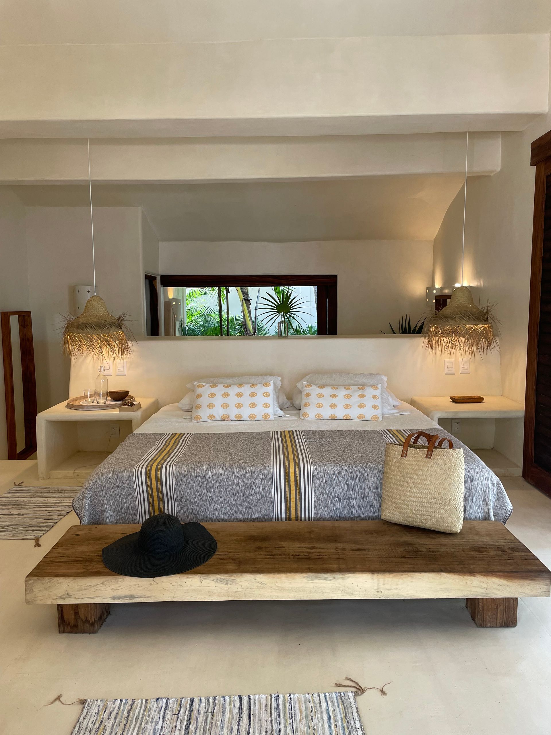 Dormitorio con paredes blancas, un banco rústico de madera a los pies de la cama y luz natural.