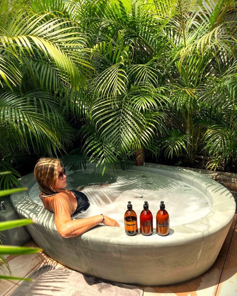 Mujer en traje de baño negro relajándose en un jacuzzi al aire libre, rodeada de plantas tropicales.