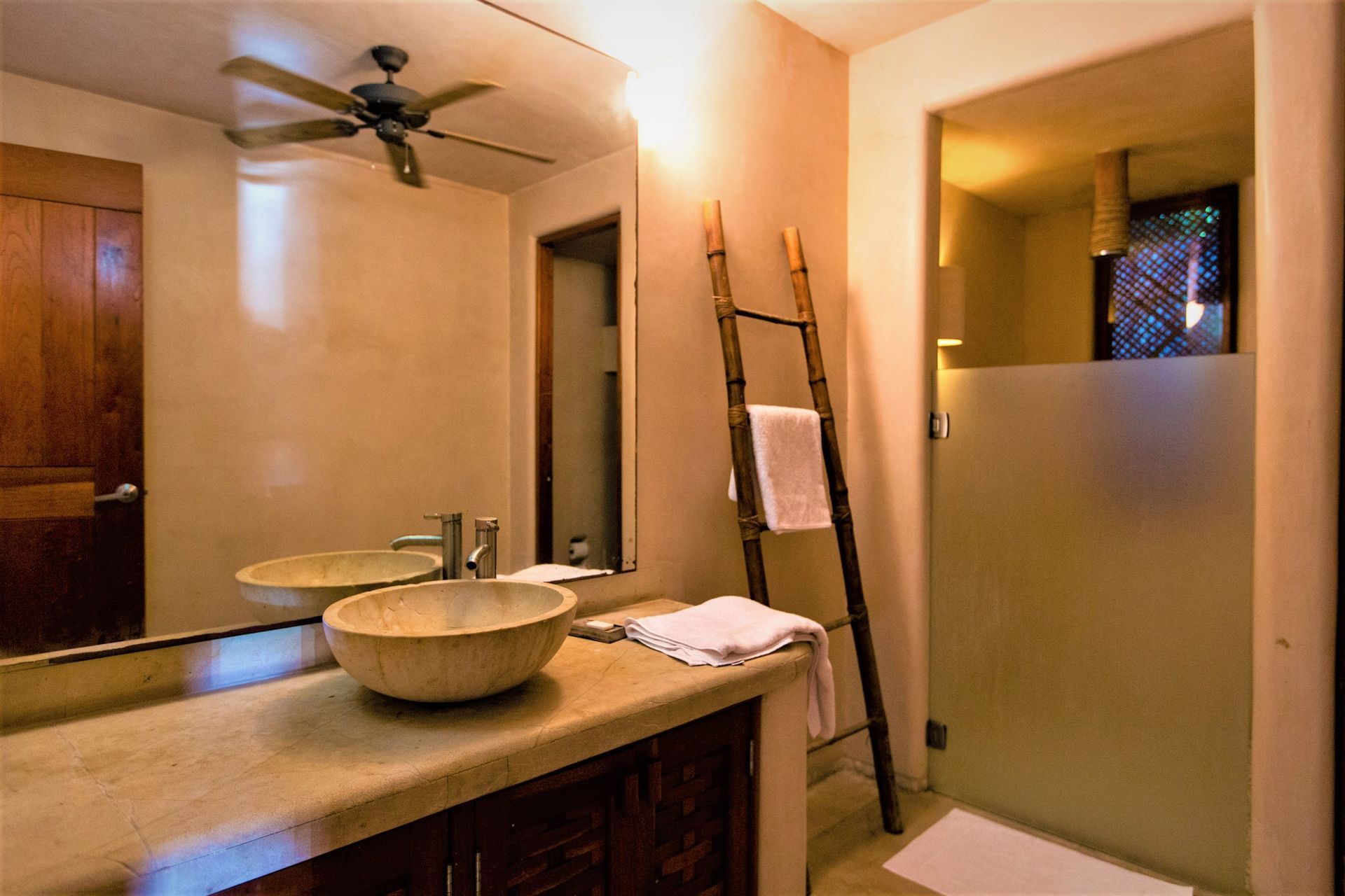 Baño con lavabo de vasija, tocador de madera, toallero de escalera y ducha de vidrio esmerilado.