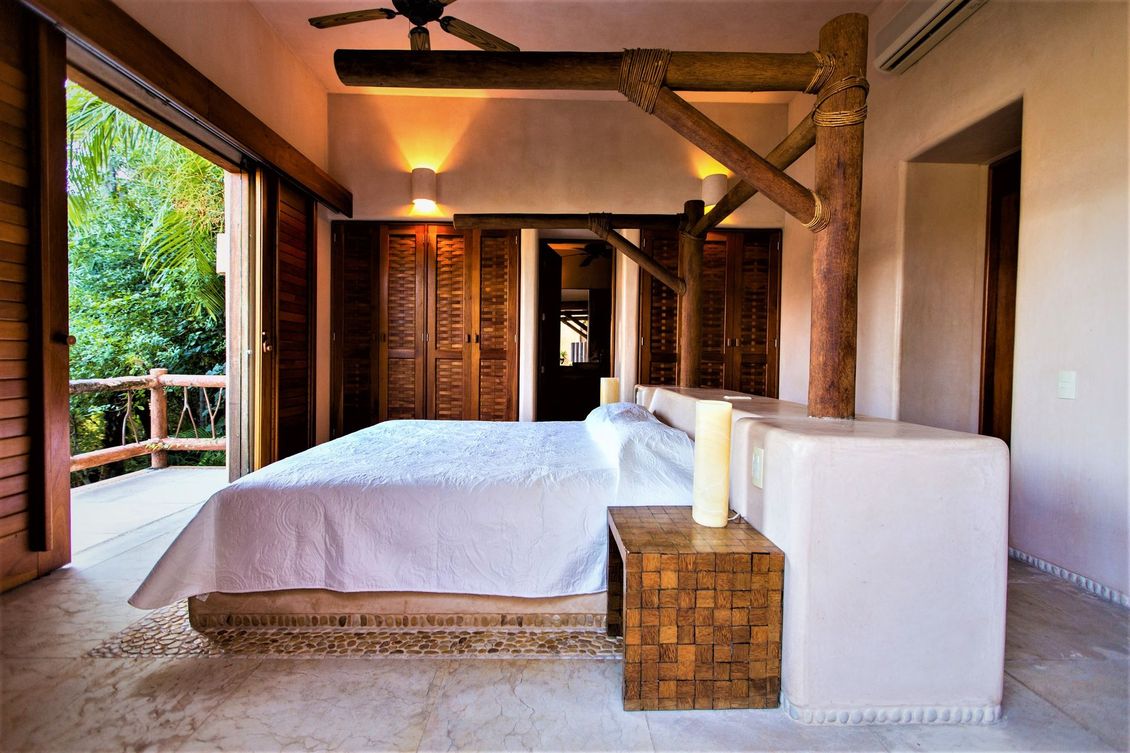 Dormitorio con ropa de cama blanca, detalles de madera y vista a un balcón verde.