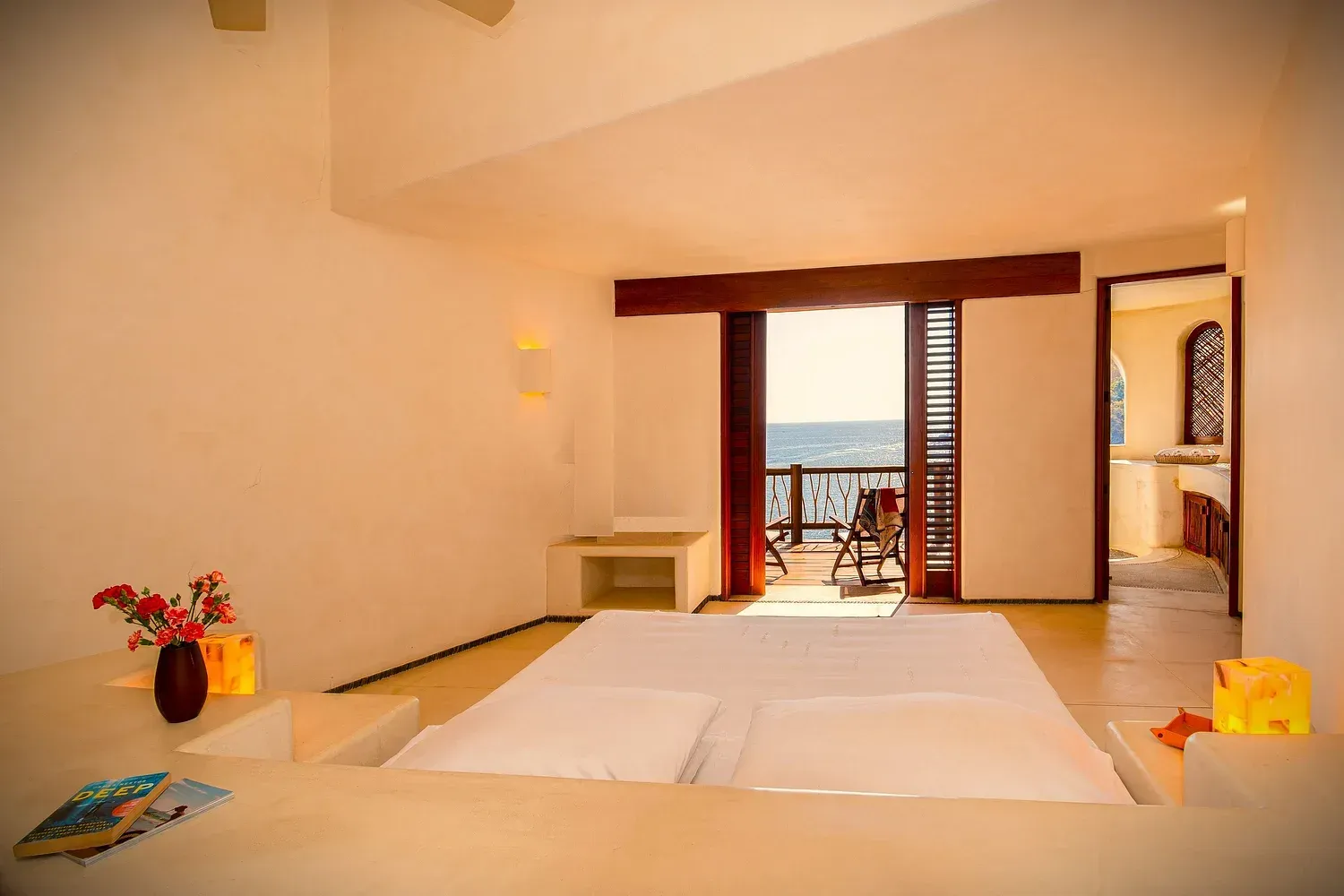 Dormitorio luminoso con cama, balcón con vistas al mar y puerta abierta que da acceso a un baño.