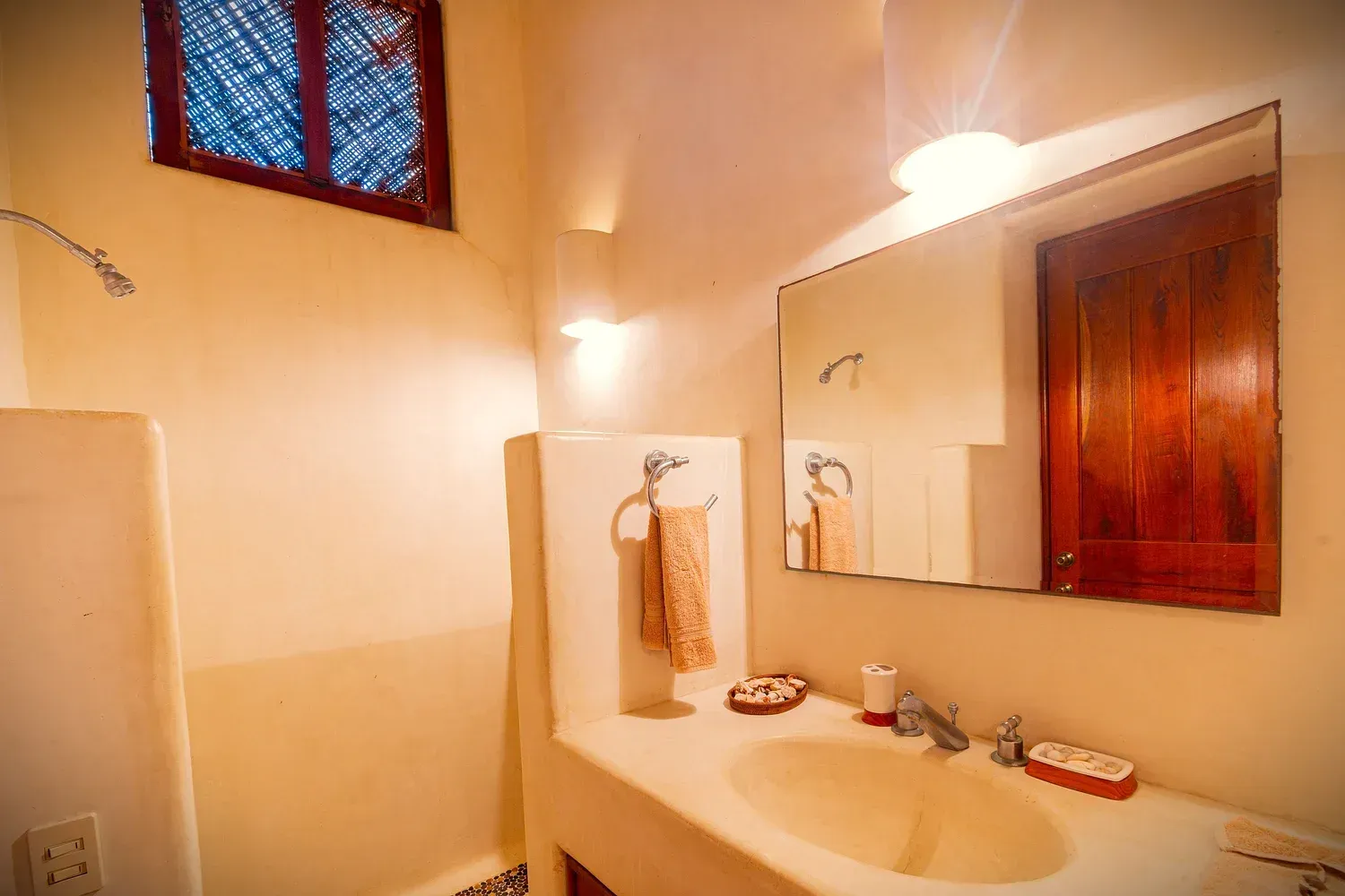 Baño con paredes blancas, lavabo, espejo y ventana pequeña. Tonos beige y marrón.