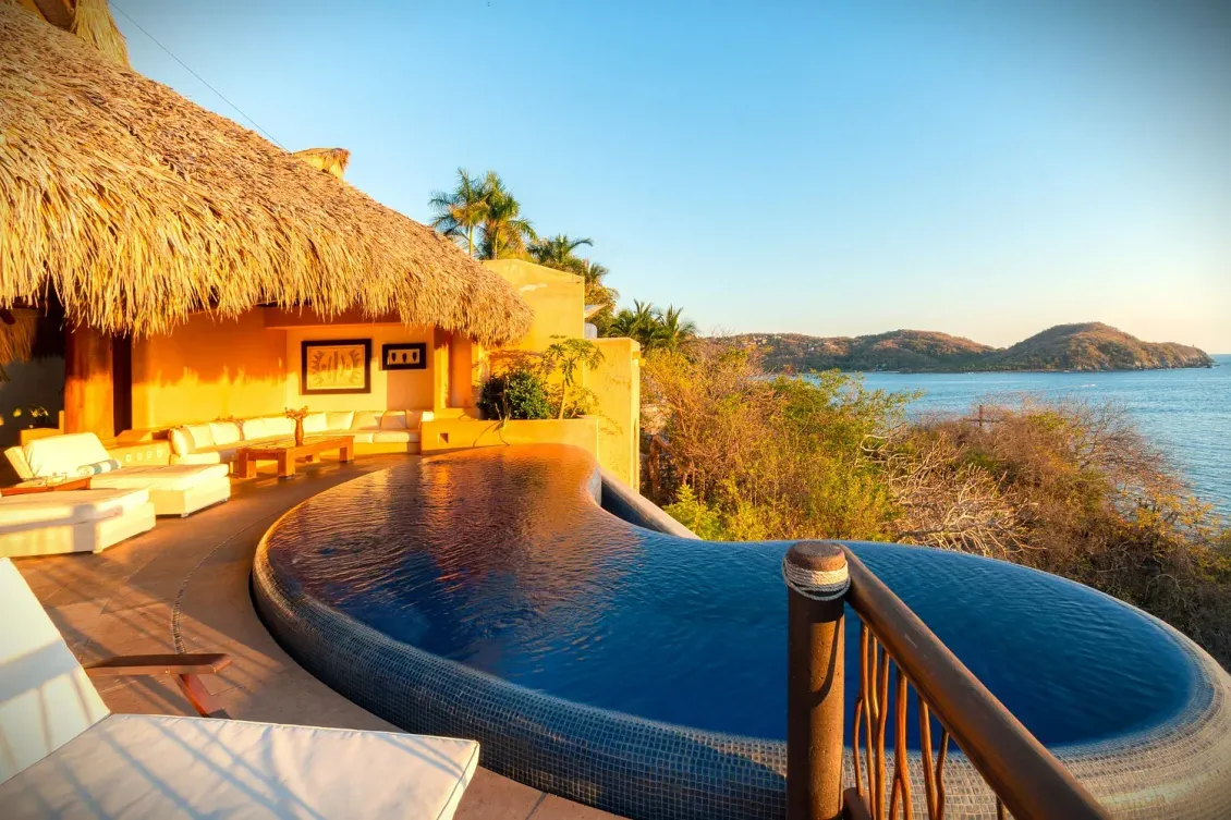 Resort de lujo con piscina infinita con vista al océano al atardecer.