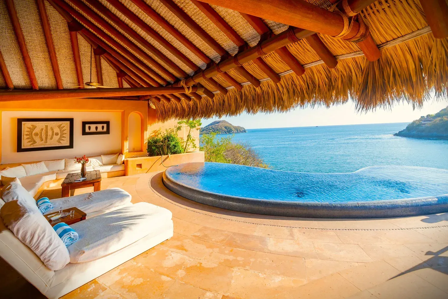 Zona de estar con piscina y vistas al océano. Muebles blancos, techo de paja y aguas azules.