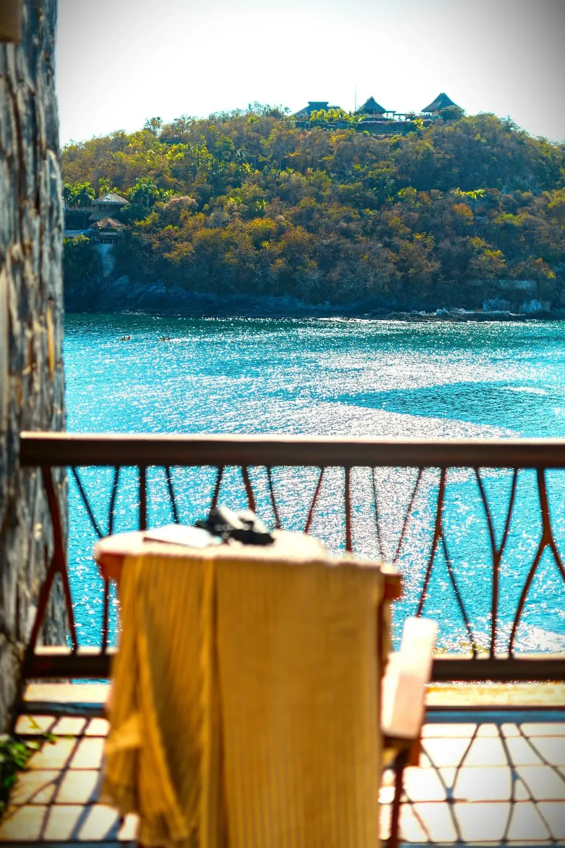 Vista desde el balcón del agua turquesa, una colina cubierta de árboles y una mesa con una toalla.