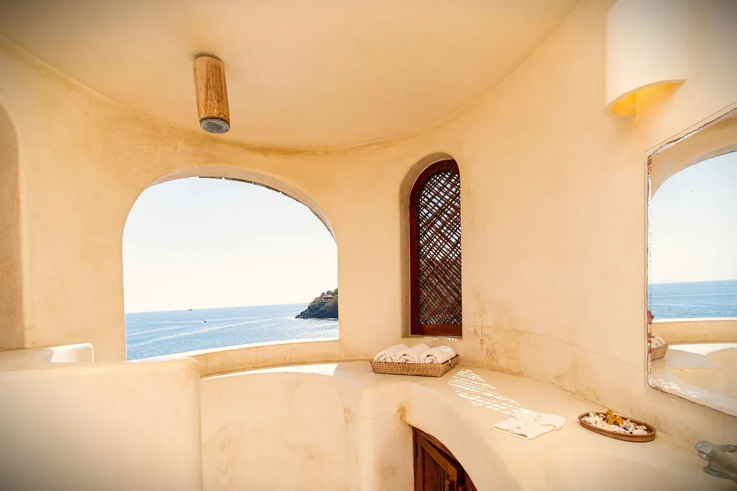 Alcoba de baño con ventana arqueada, vista al mar y decoración rústica.
