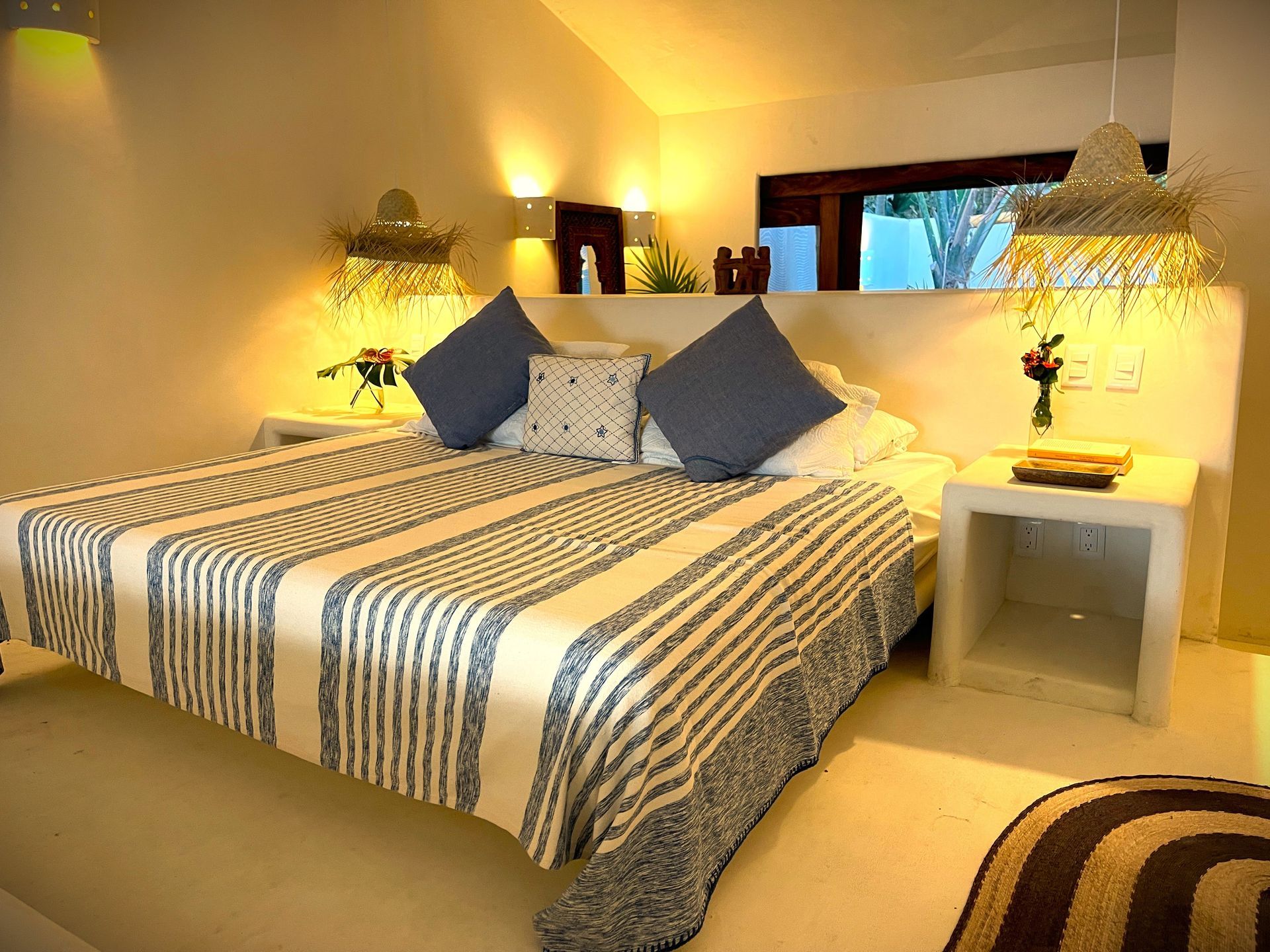 Dormitorio con manta de rayas, almohadas azules, paredes blancas y lámparas decorativas.