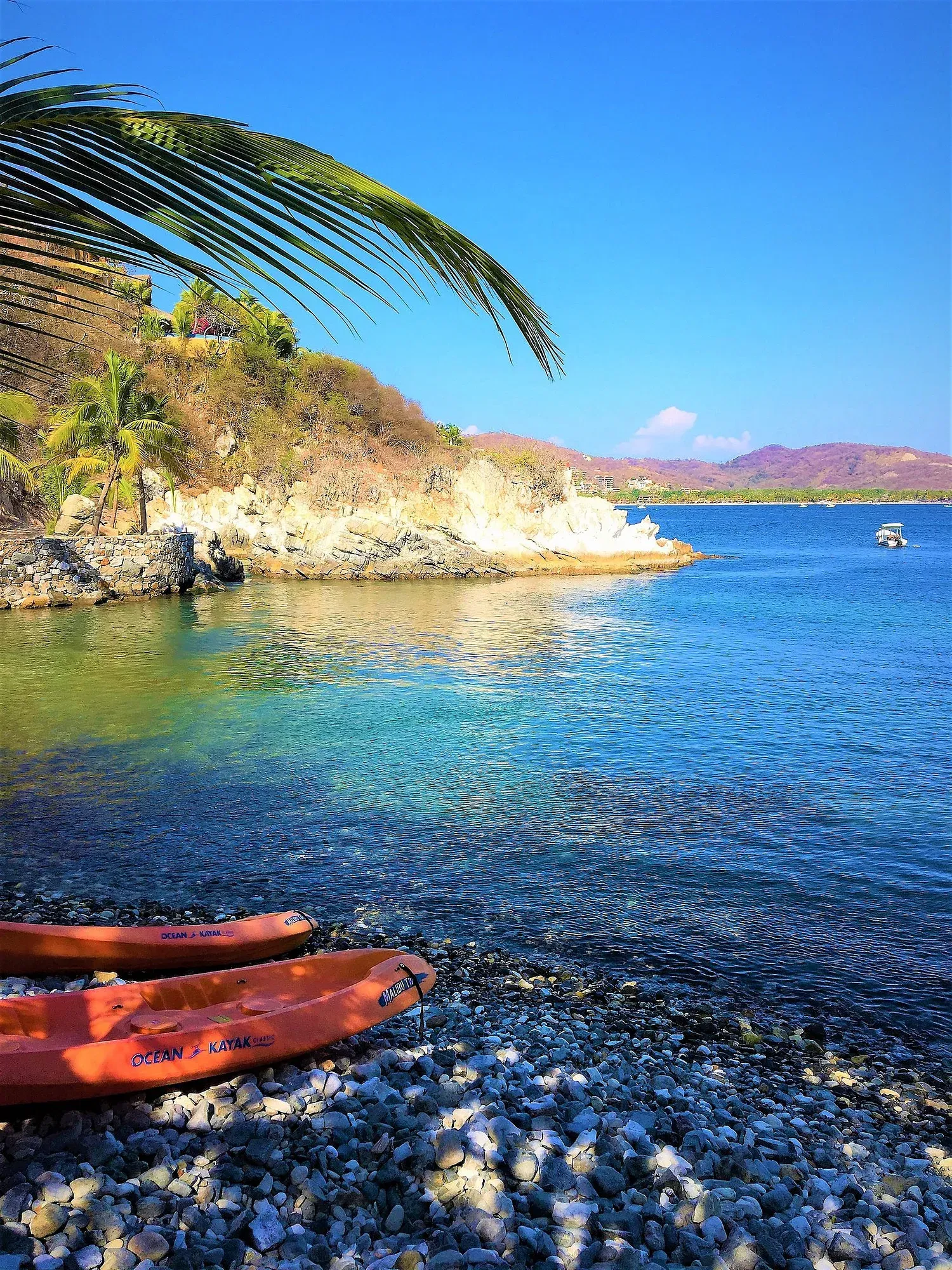 Kayaks naranjas en una playa rocosa con agua turquesa clara bajo un cielo soleado.