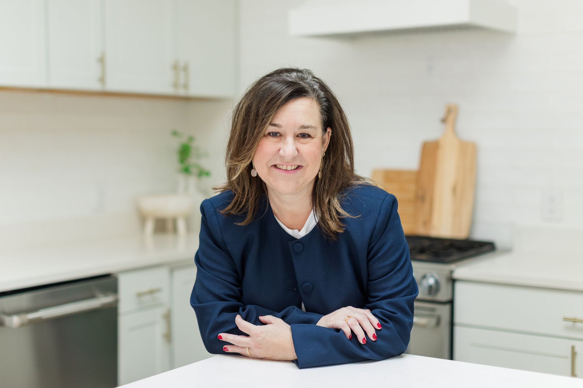 Woman smiling at a kitchen counter in a bright modern kitchen, wearing a navy blazer.
