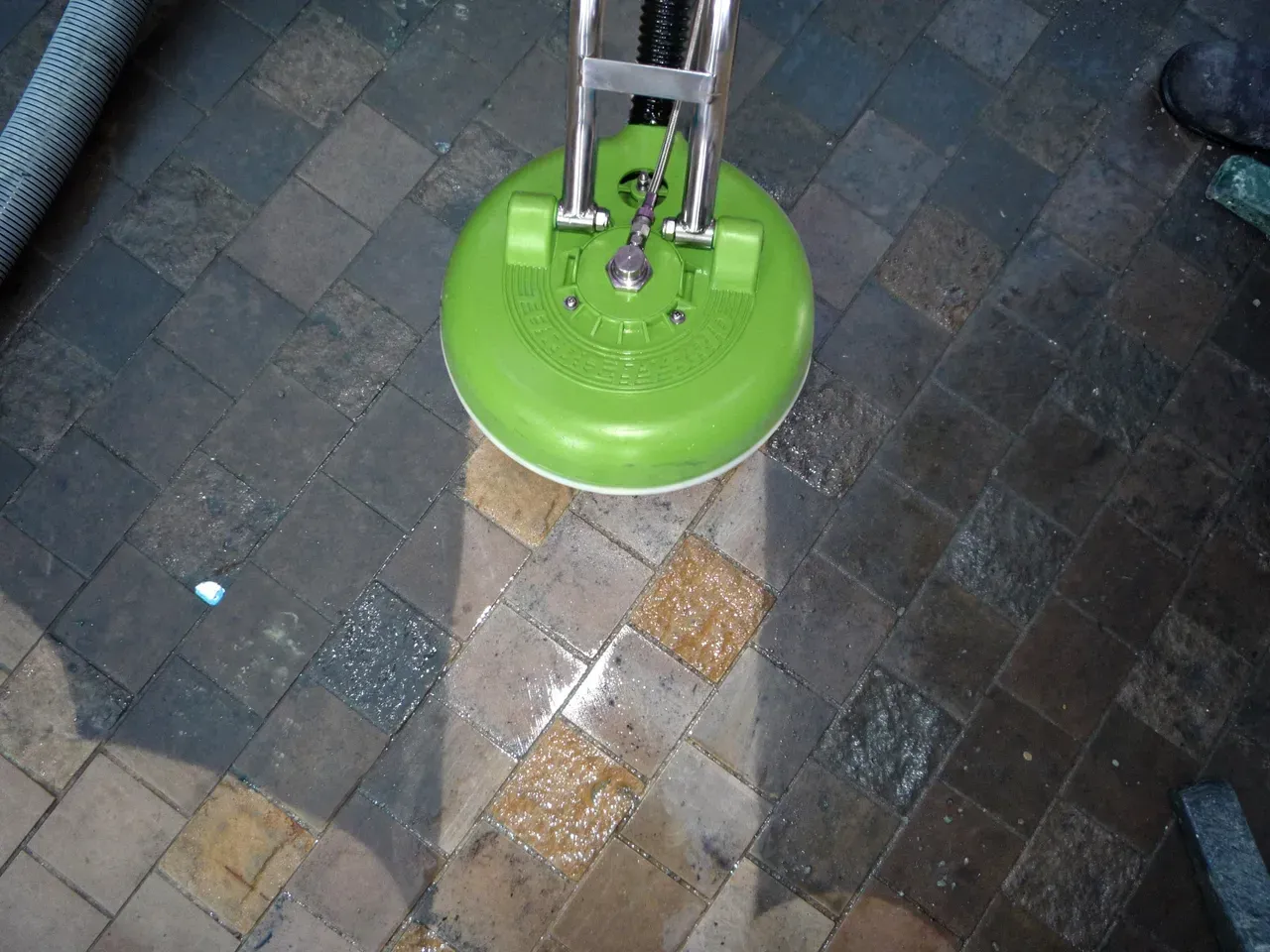 A green surface cleaner being used on a brick patio, cleaning visible in the wet area.