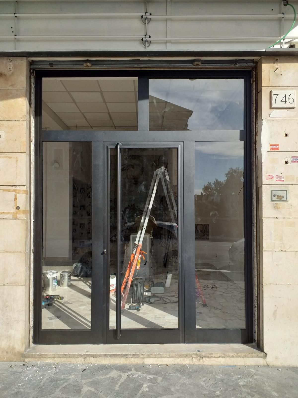 Vetrina d'ingresso con doppie porte e scala visibile all'interno, spazio vuoto.