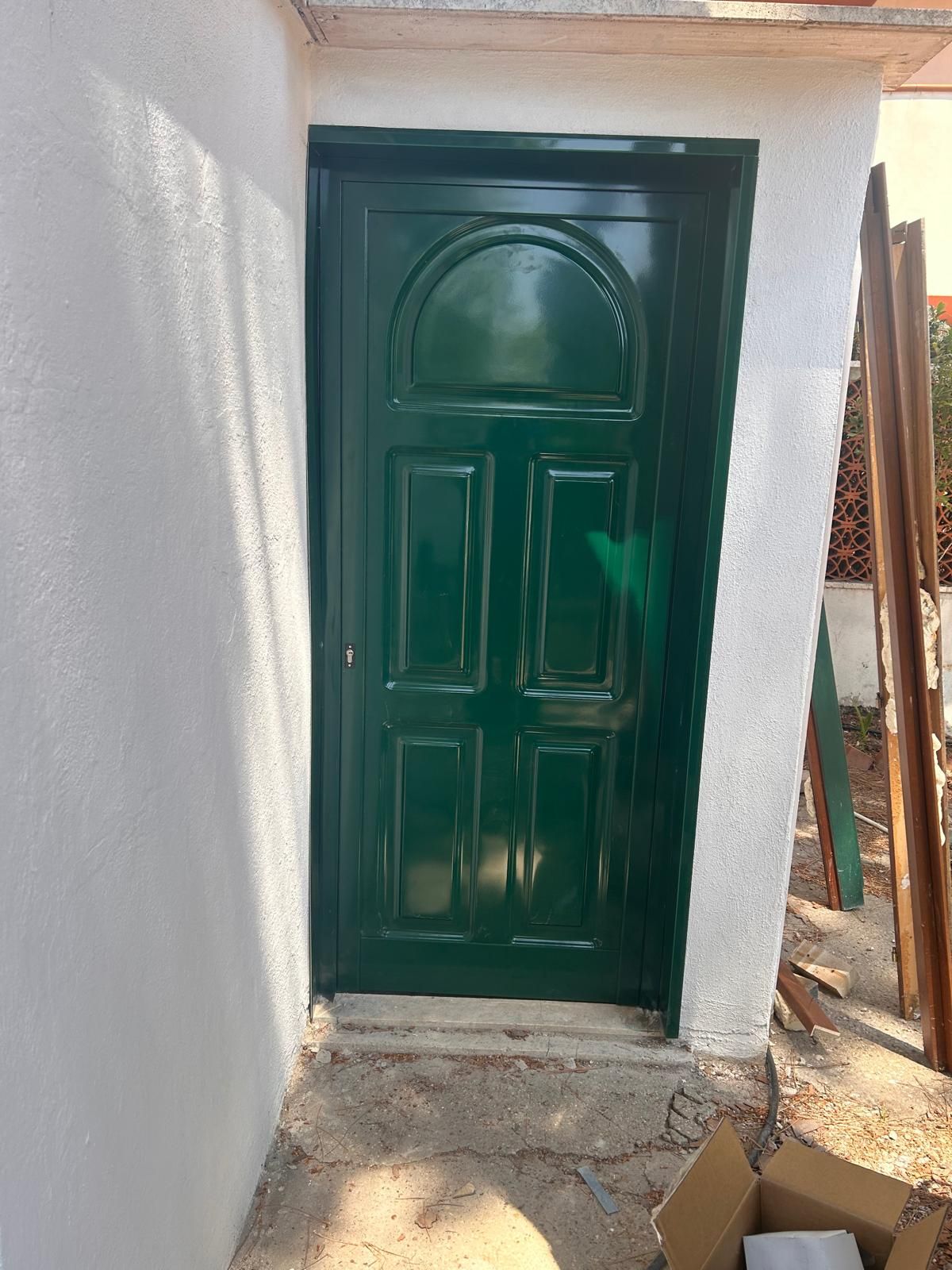 Porta d'ingresso verde incastonata in una parete di stucco bianco, visibile attraverso uno stretto passaggio esterno.