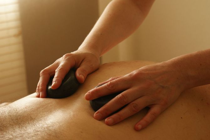 Hands performing a hot stone massage on a person’s back in a warm spa setting