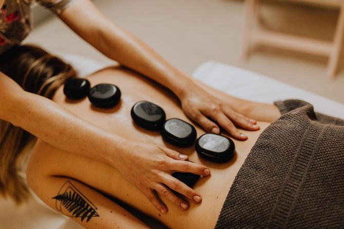 Hot stone massage on a client’s back in a spa, with hands applying the stones and a towel nearby