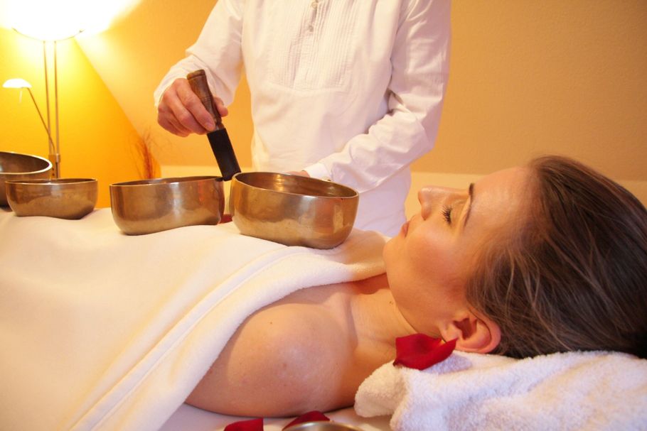 Spa therapist using singing bowls over a woman lying on a massage table with a white towel