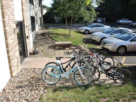 Bicycles parked on grass beside an apartment building and parking lot.