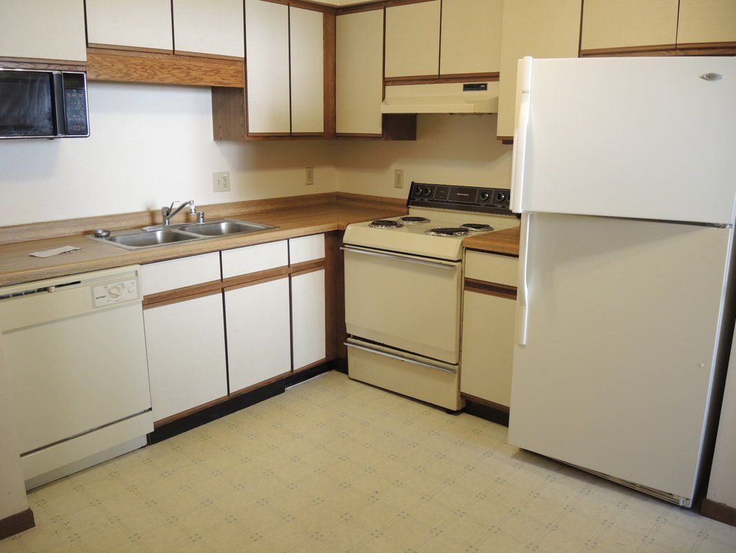 Small kitchen with white appliances, wood cabinets, and beige flooring.
