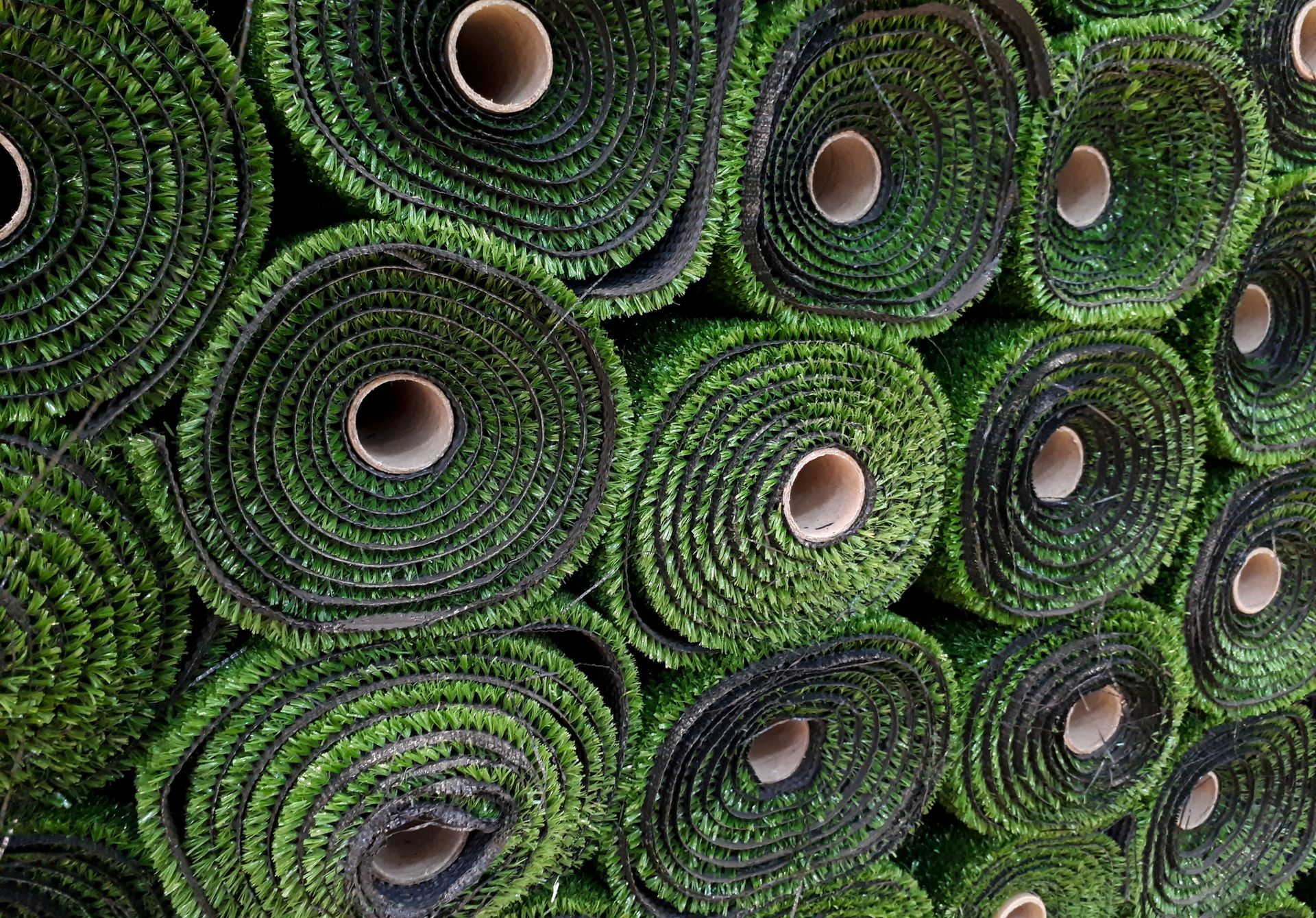 Rotoli impilati di erba sintetica di un verde brillante, che mostrano le estremità circolari e l'anima centrale in cartone.