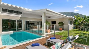 Poolside view of a modern house with pool, patio, lawn, and mountain backdrop on a sunny day.