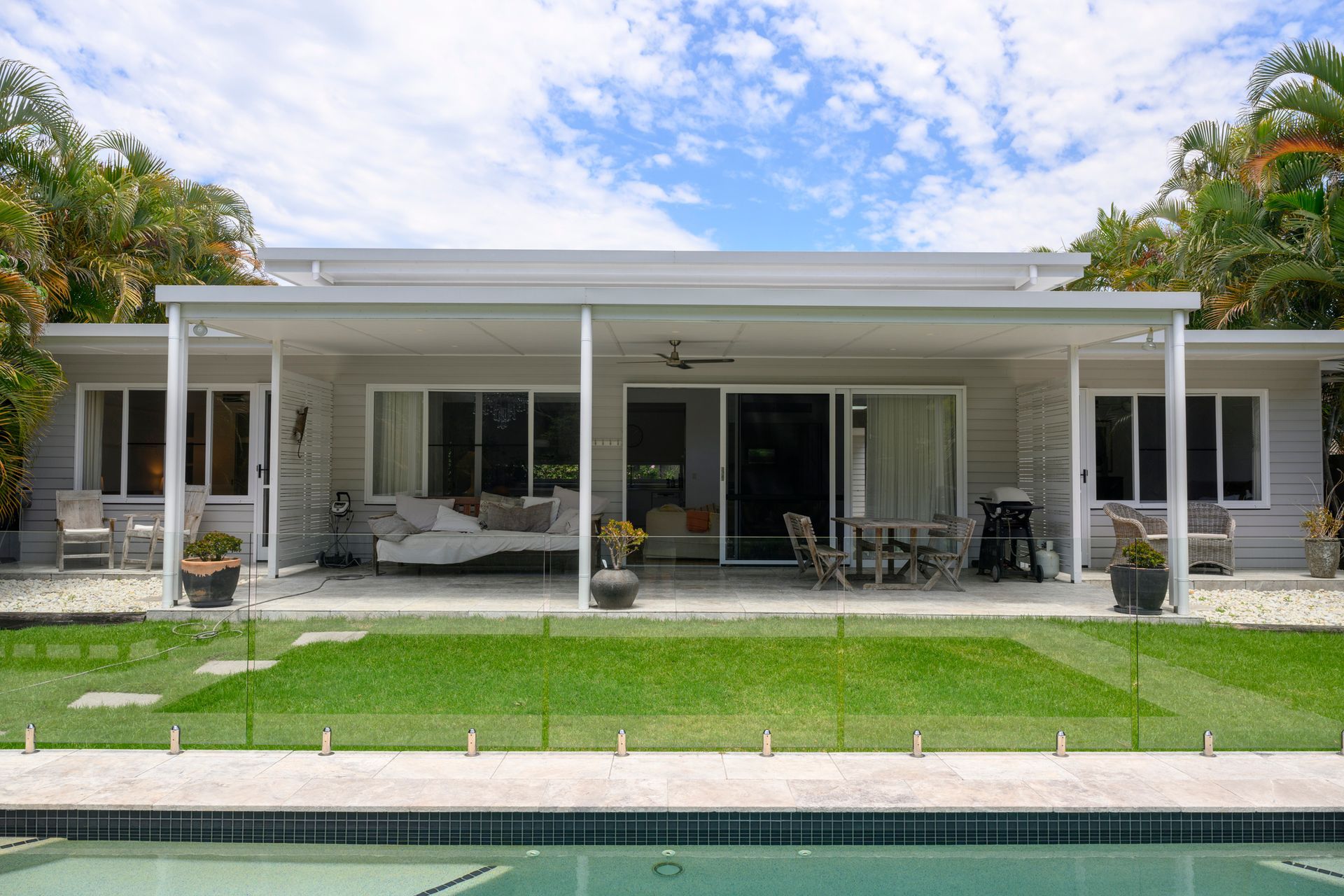 View across swimming pool enclosed in glass, green lawn, covered patio, and outdoor furniture. View across swimming pool enclosed in glass, green lawn, covered patio, and outdoor furniture.
