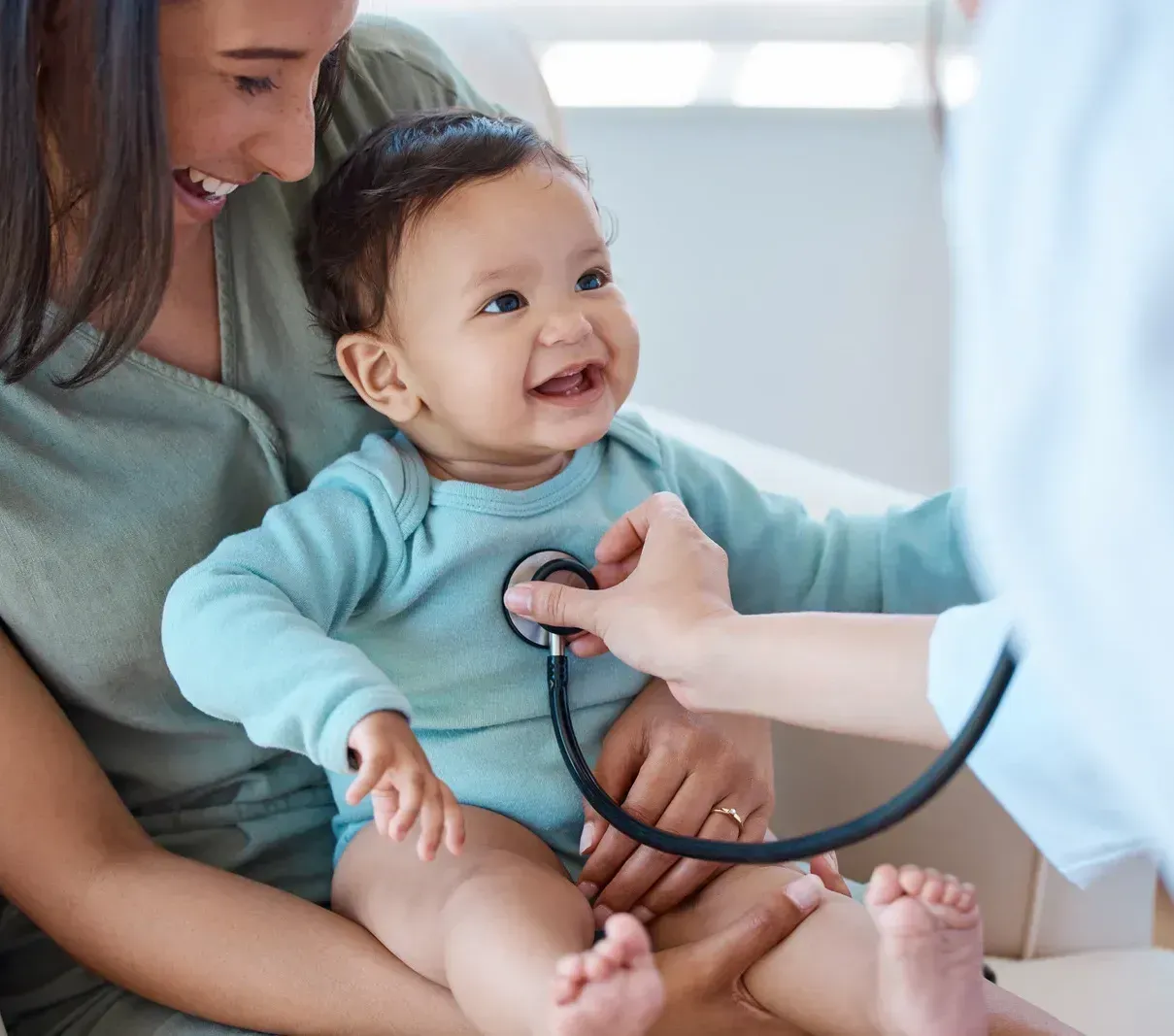 Baby smiling as a doctor checks their chest with a stethoscope while a parent holds them nearby
