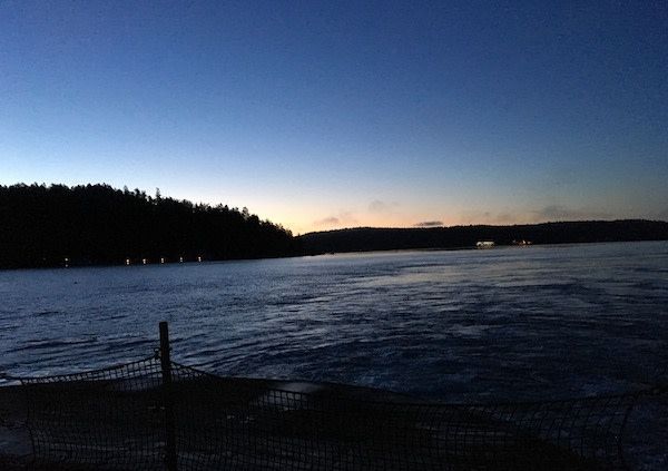 A large body of water with a fence in the foreground and a sunset in the background.