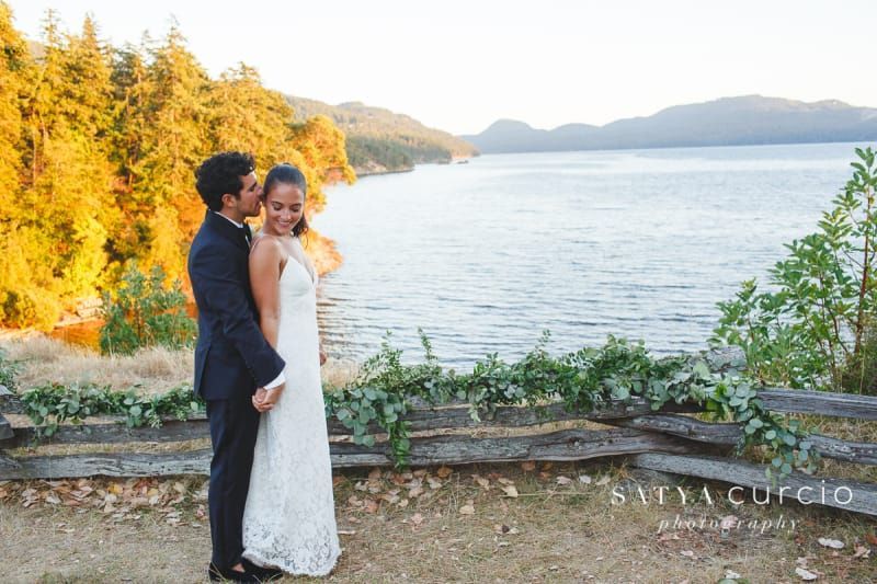 A bride and groom are posing for a picture in front of a lake.