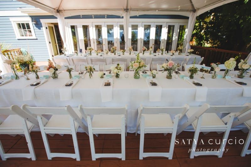 A long white table with white chairs under a tent